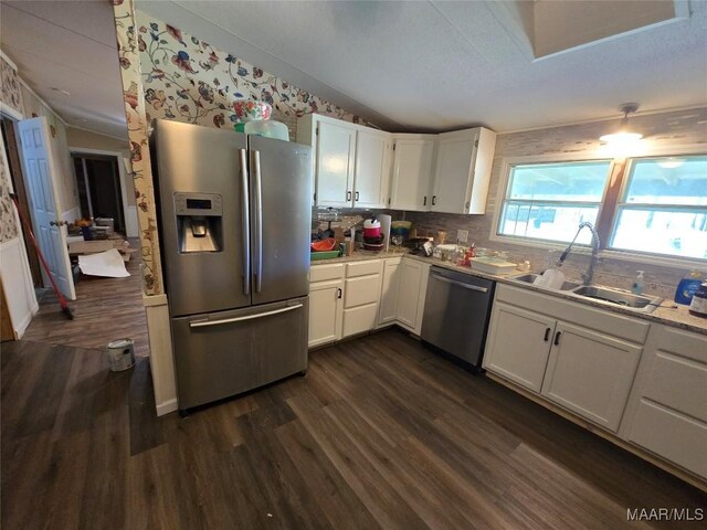 kitchen with a sink, dark wood finished floors, lofted ceiling, stainless steel appliances, and white cabinets