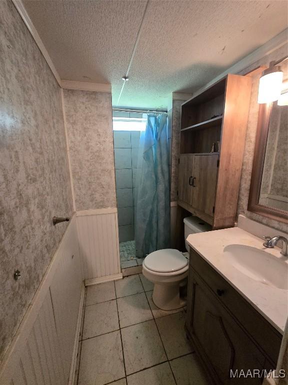 full bath with tile patterned flooring, toilet, a shower stall, a textured ceiling, and a wainscoted wall