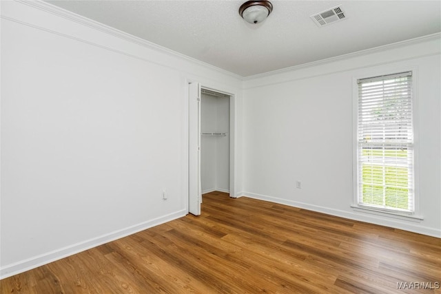 unfurnished bedroom with baseboards, wood finished floors, visible vents, and crown molding