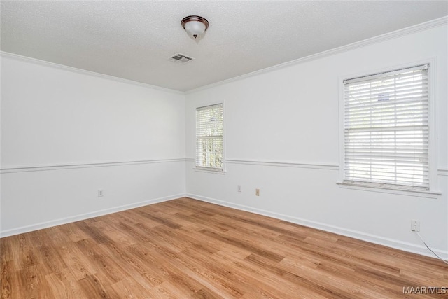 spare room with light wood-style floors, visible vents, a textured ceiling, and ornamental molding