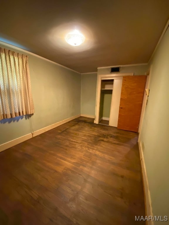 unfurnished bedroom featuring a closet, dark wood finished floors, baseboards, ornamental molding, and visible vents