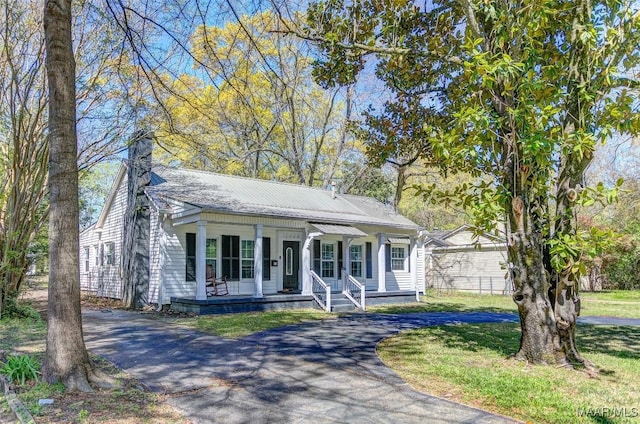 view of front of house featuring metal roof, covered porch, a chimney, aphalt driveway, and a front lawn