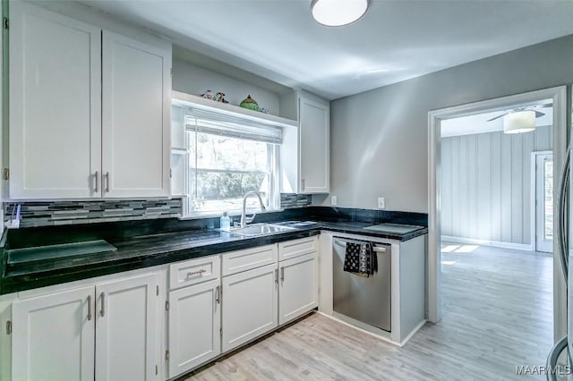 kitchen featuring light wood-type flooring, white cabinetry, dark countertops, stainless steel dishwasher, and a sink