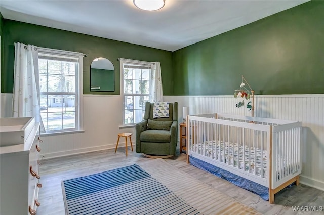 bedroom with multiple windows, wainscoting, and wood finished floors
