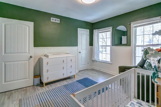 bedroom with visible vents, light wood-style flooring, and wainscoting