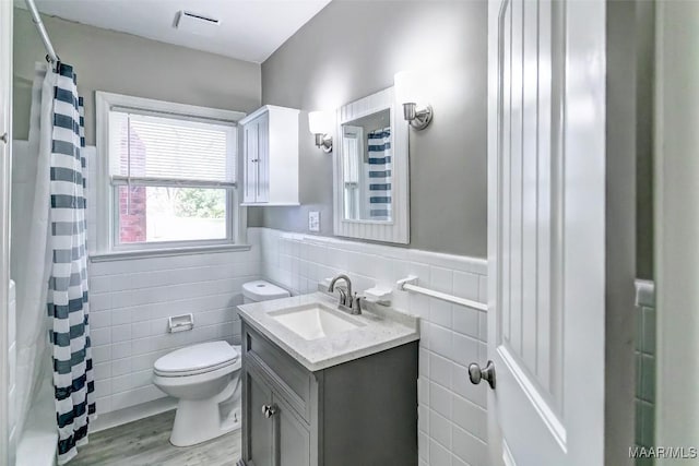 bathroom with vanity, toilet, wainscoting, tile walls, and wood finished floors