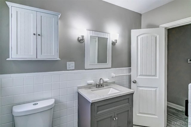 bathroom with toilet, vanity, a wainscoted wall, and tile walls
