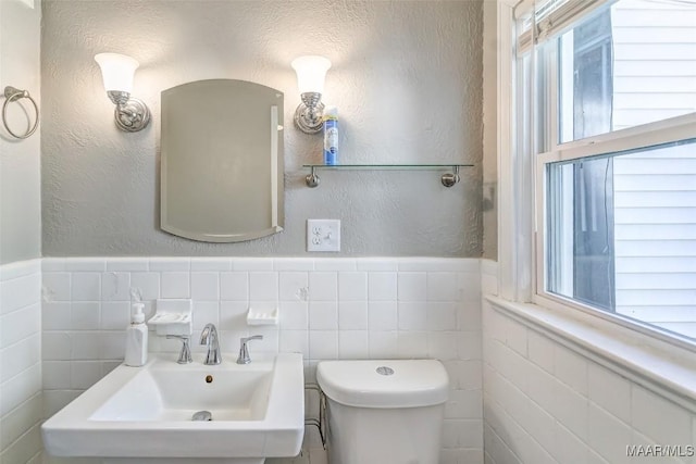 half bathroom with toilet, a textured wall, a sink, and wainscoting