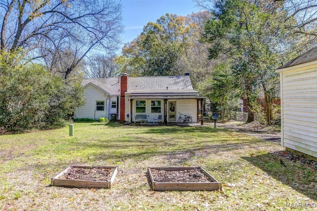back of property with a chimney, a garden, metal roof, a lawn, and covered porch