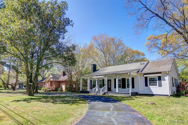 view of front of house with a chimney, covered porch, a front yard, and driveway