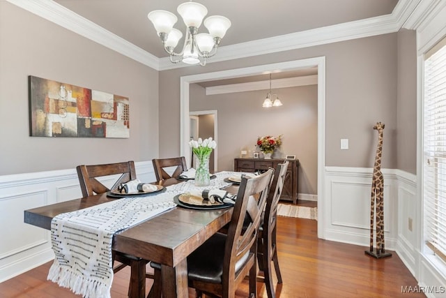 dining room featuring ornamental molding, wainscoting, wood finished floors, and a notable chandelier