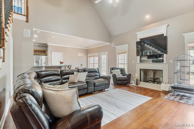 living area with high vaulted ceiling, ceiling fan with notable chandelier, wood finished floors, a high end fireplace, and ornamental molding