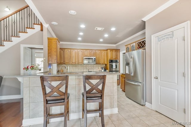 kitchen featuring visible vents, ornamental molding, a peninsula, baseboards, and stainless steel appliances