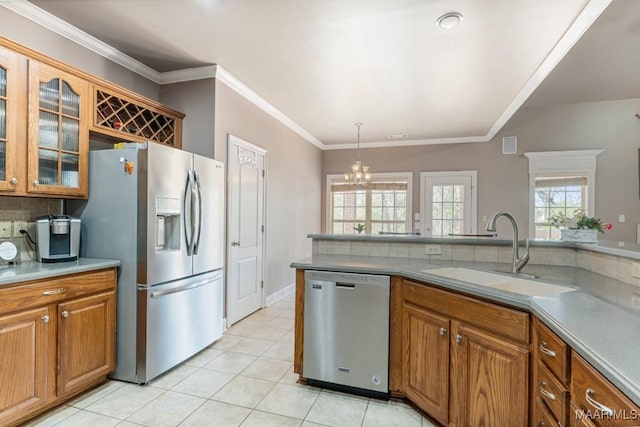 kitchen featuring brown cabinetry, appliances with stainless steel finishes, a sink, a notable chandelier, and glass insert cabinets