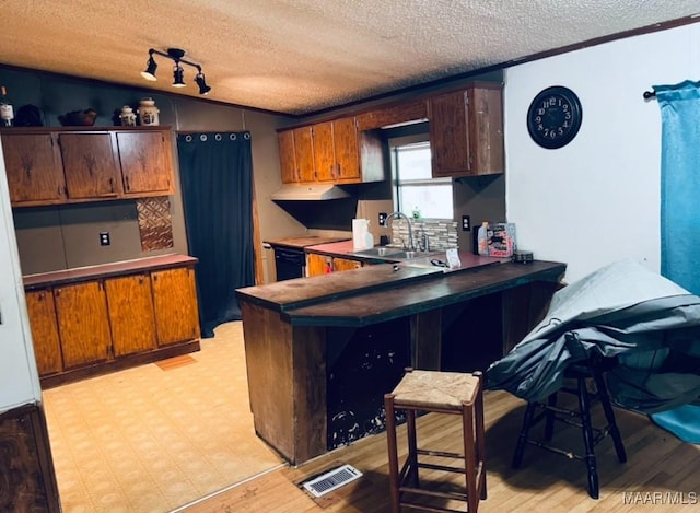 kitchen with a sink, a textured ceiling, light wood-style floors, a peninsula, and ventilation hood