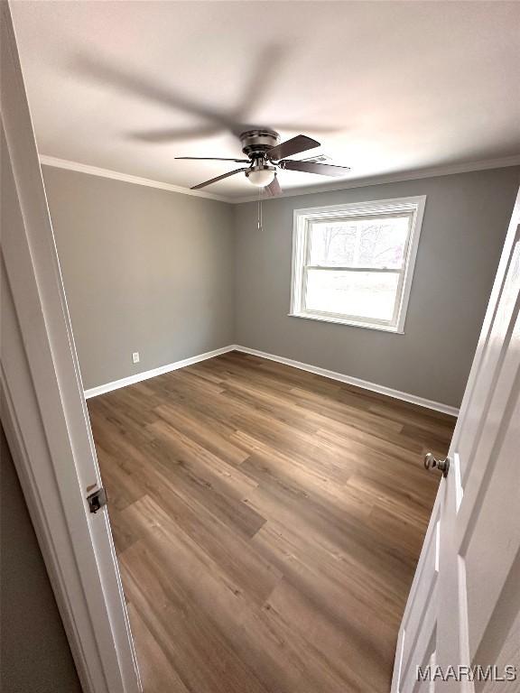 spare room featuring dark wood-type flooring, crown molding, ceiling fan, and baseboards