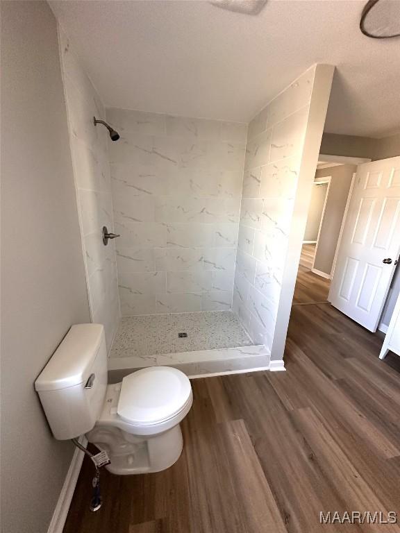 full bathroom with toilet, a stall shower, wood finished floors, and baseboards