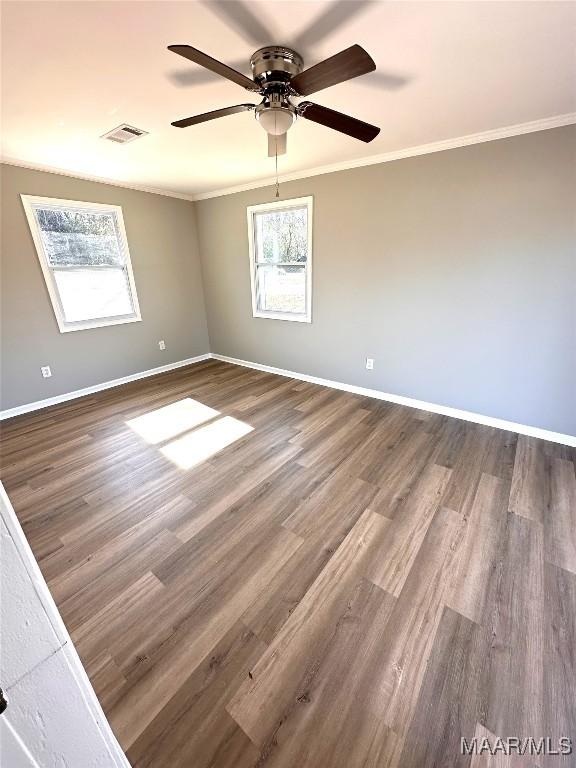 spare room with baseboards, crown molding, visible vents, dark wood finished floors, and ceiling fan