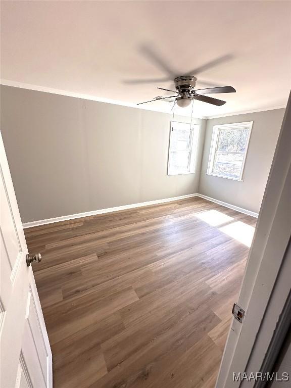 spare room featuring baseboards, ornamental molding, a ceiling fan, and wood finished floors