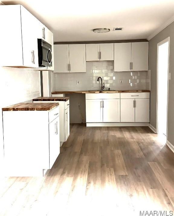 kitchen featuring tasteful backsplash, white cabinets, a sink, stainless steel microwave, and wood finished floors