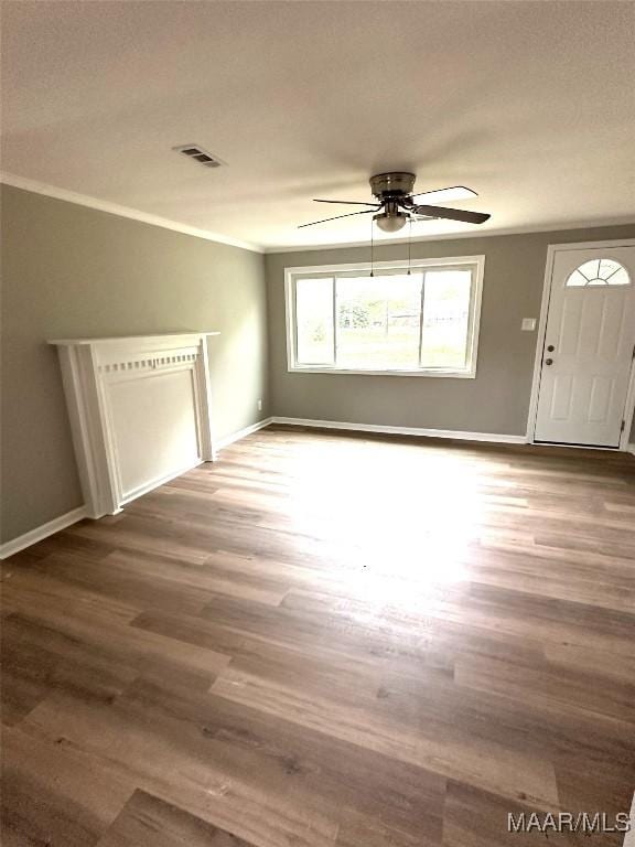 unfurnished living room featuring visible vents, baseboards, ornamental molding, a ceiling fan, and wood finished floors
