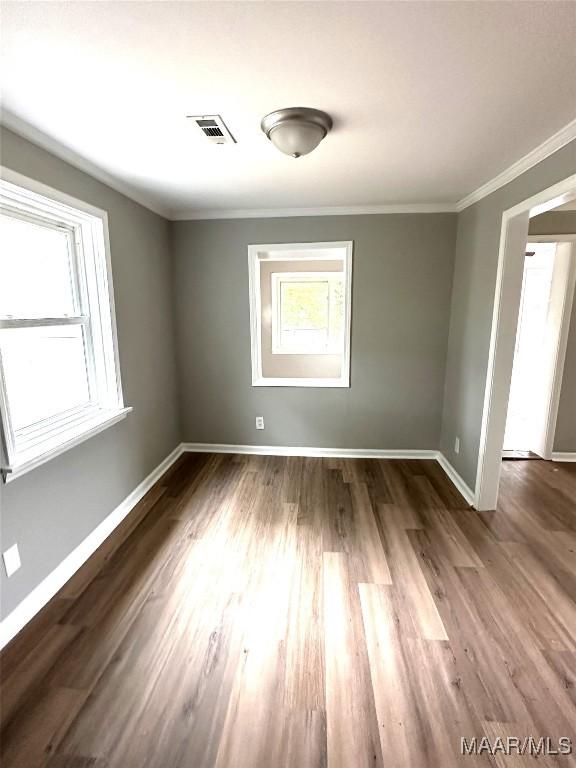 empty room with wood finished floors, baseboards, ornamental molding, and visible vents