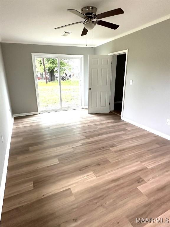 empty room featuring wood finished floors, baseboards, a ceiling fan, and visible vents