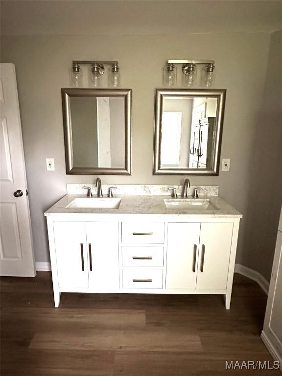full bath featuring double vanity, baseboards, a sink, and wood finished floors