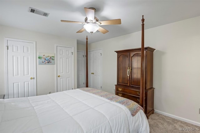 bedroom featuring visible vents, two closets, baseboards, ceiling fan, and light colored carpet
