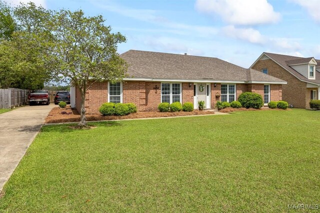view of front facade with a front yard, concrete driveway, fence, brick siding, and a shingled roof