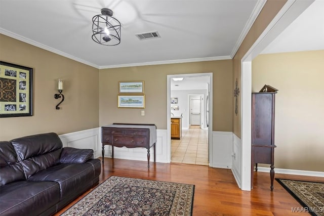 living room featuring wainscoting, light wood-style flooring, crown molding, and visible vents