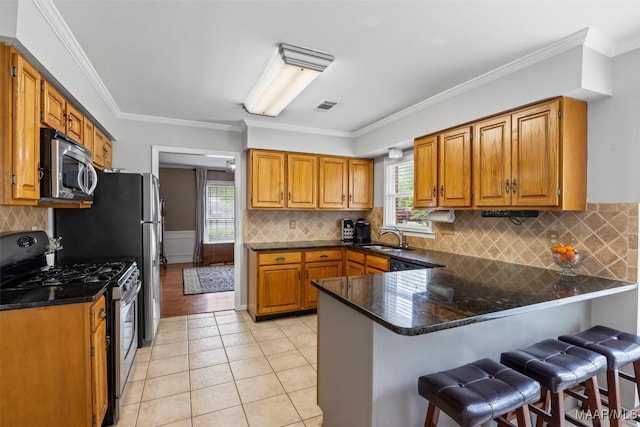 kitchen with light tile patterned floors, stainless steel appliances, visible vents, a peninsula, and brown cabinetry
