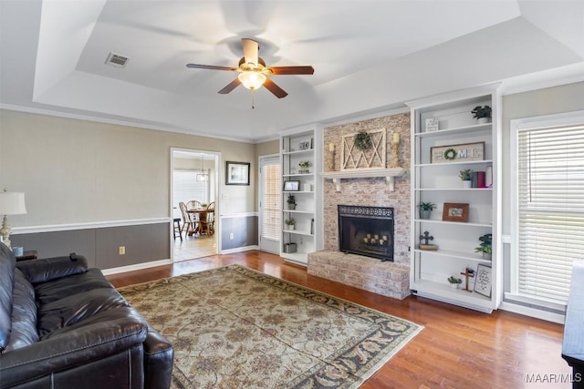 living area featuring a healthy amount of sunlight, a raised ceiling, visible vents, a ceiling fan, and wood finished floors