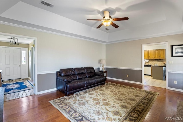 living area featuring a tray ceiling, crown molding, a ceiling fan, visible vents, and light wood-style floors
