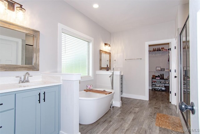 bathroom featuring wood finished floors, a freestanding tub, vanity, a walk in closet, and recessed lighting