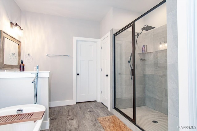 bathroom with a shower stall, wood finished floors, a freestanding bath, vanity, and baseboards