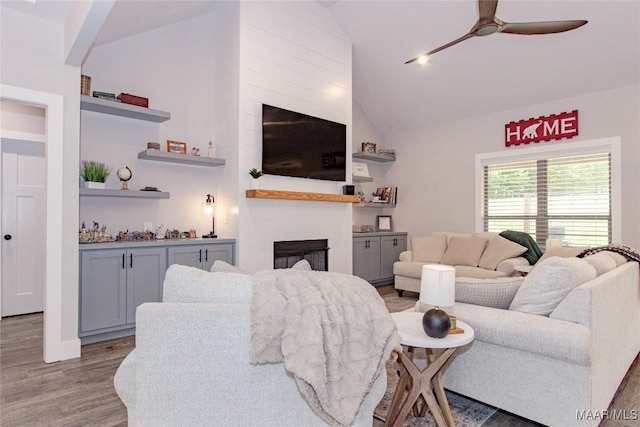 living area with ceiling fan, light wood finished floors, high vaulted ceiling, and a glass covered fireplace