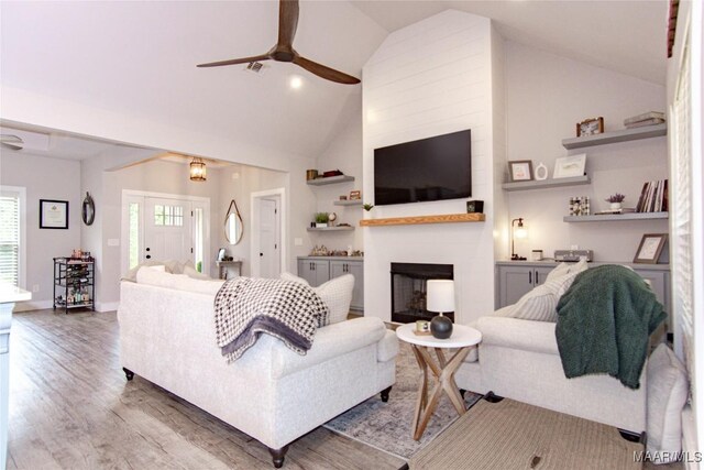 living room with a ceiling fan, wood finished floors, a large fireplace, high vaulted ceiling, and baseboards