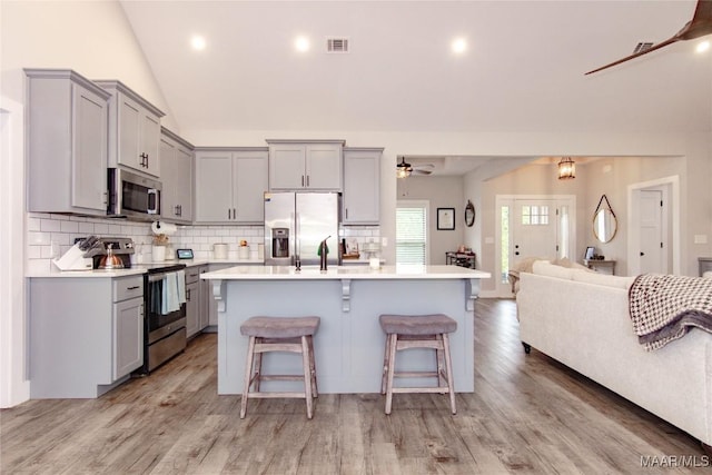 kitchen featuring stainless steel appliances, gray cabinetry, ceiling fan, light wood-type flooring, and a breakfast bar