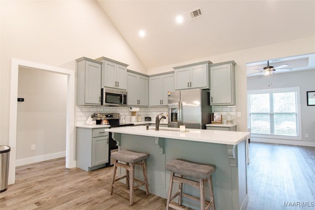 kitchen featuring appliances with stainless steel finishes, gray cabinets, light wood-style floors, recessed lighting, and high vaulted ceiling