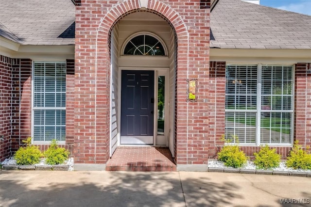 property entrance featuring brick siding and a shingled roof