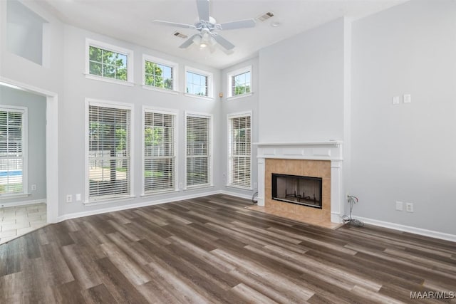 unfurnished living room featuring ceiling fan, a high ceiling, wood finished floors, a tile fireplace, and baseboards