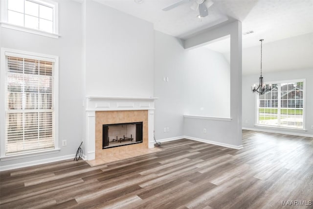 unfurnished living room with a ceiling fan, a tile fireplace, wood finished floors, a chandelier, and baseboards
