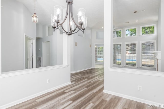 unfurnished dining area with a chandelier, wood finished floors, healthy amount of natural light, baseboards, and a towering ceiling