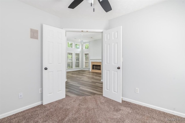 carpeted empty room with a ceiling fan, baseboards, and a tile fireplace