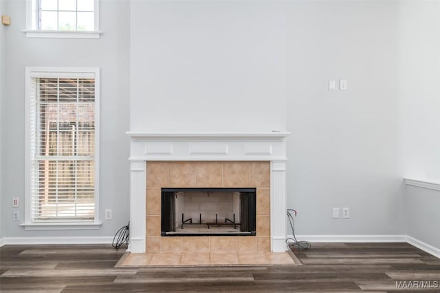 detailed view of a tiled fireplace, wood finished floors, and baseboards