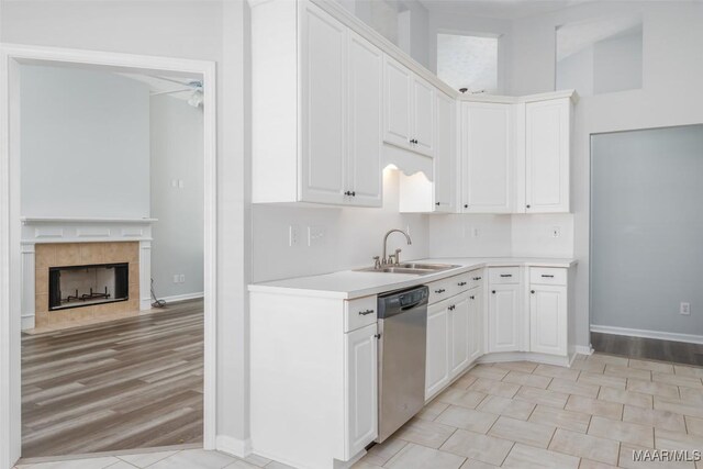 kitchen with dishwasher, a sink, baseboards, light countertops, and white cabinets