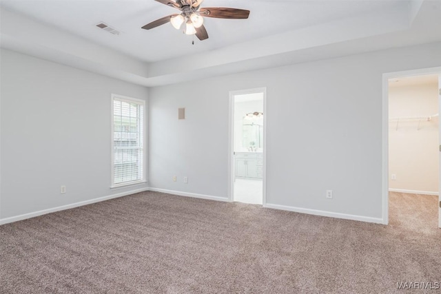 unfurnished bedroom with a raised ceiling, carpet, baseboards, and a walk in closet