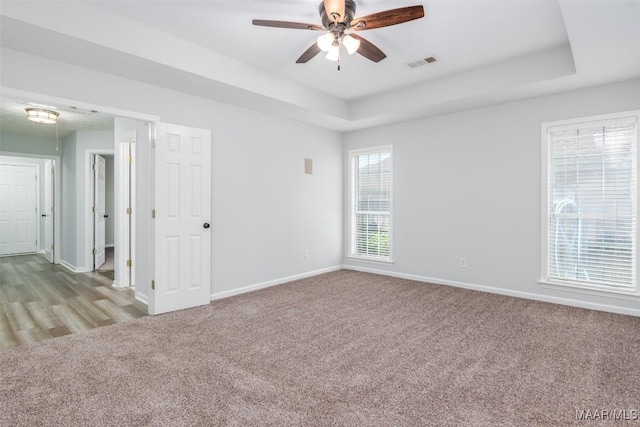empty room featuring a raised ceiling, ceiling fan, baseboards, and carpet flooring