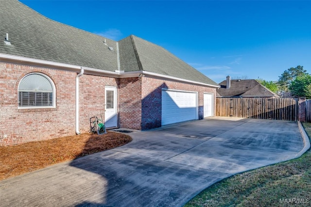 view of property exterior with fence, brick siding, an attached garage, a shingled roof, and concrete driveway